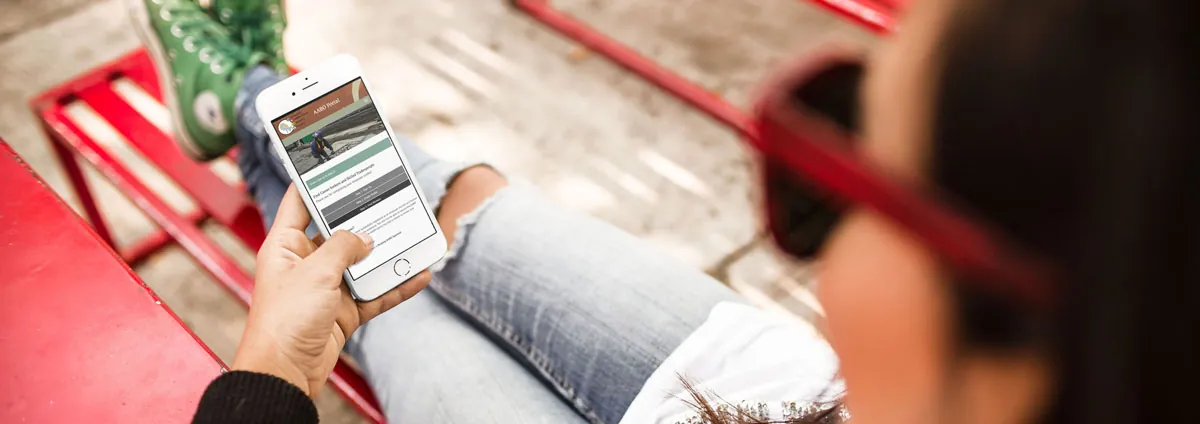 A person on a red bench holding an iPhone that shows the AABO Portal