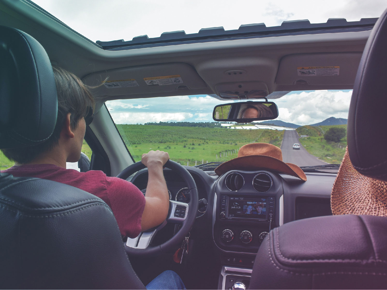 A man driving an SUV down a country road, seen from the back seat