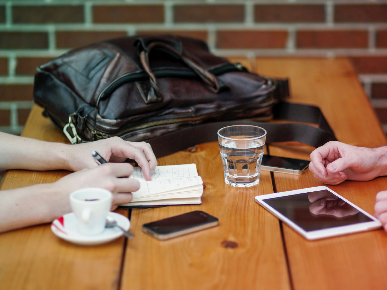 Two people at a wooden table with a notebook, coffee, phones and a tablet