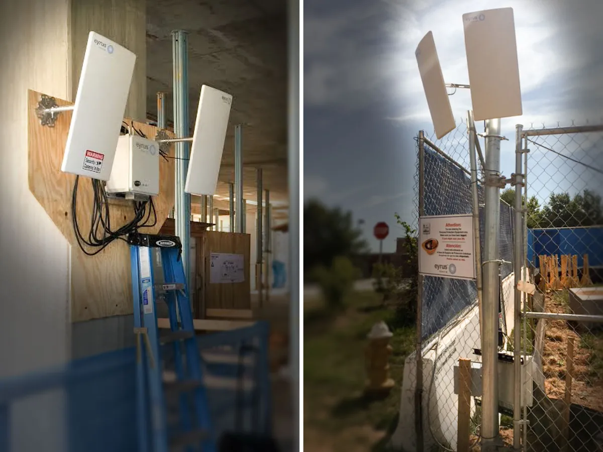 Two installed Eyrus units with flat antennas, one on plywood inside a building under construction, one on a chain-link fence