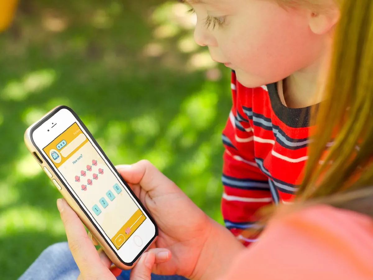 A child outdoors holding an iPhone, playing a Math Star counting question that asks "How many?"