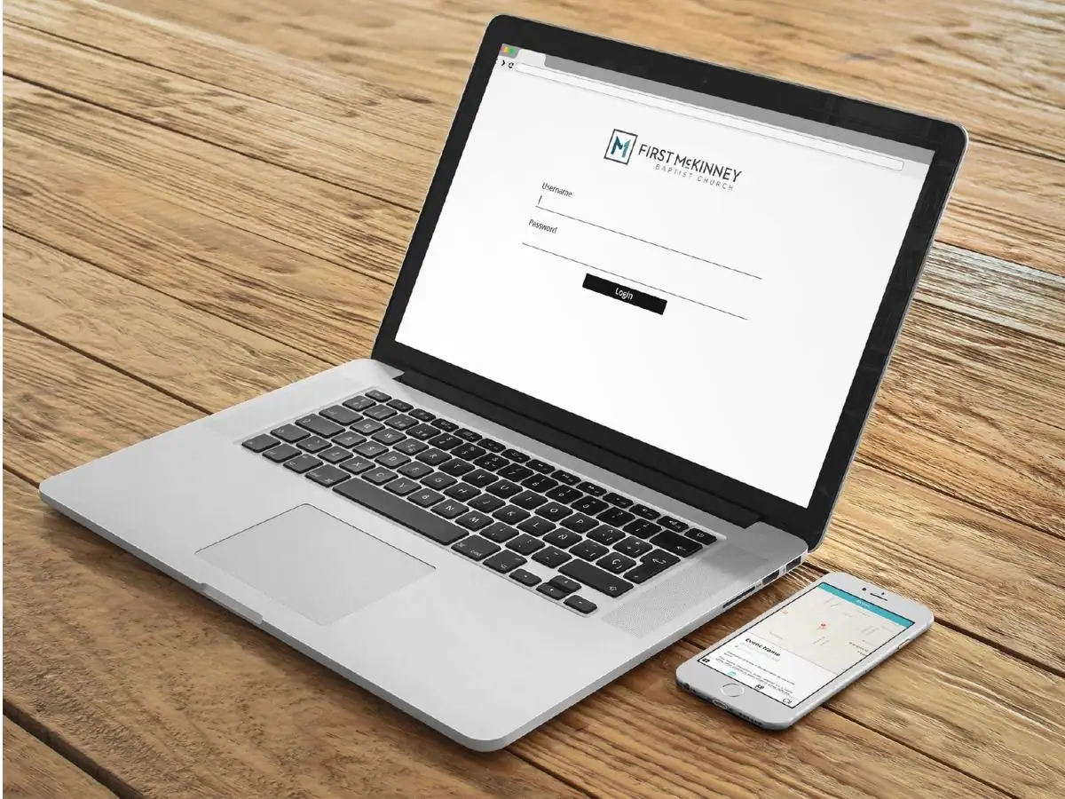 A laptop on a wooden table showing a First McKinney Baptist Church login page, next to a phone showing an event in the app