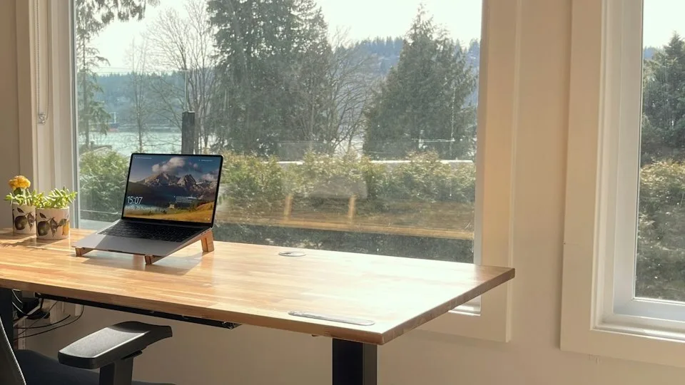 A laptop on a desk in front of a window looking out over trees and water
