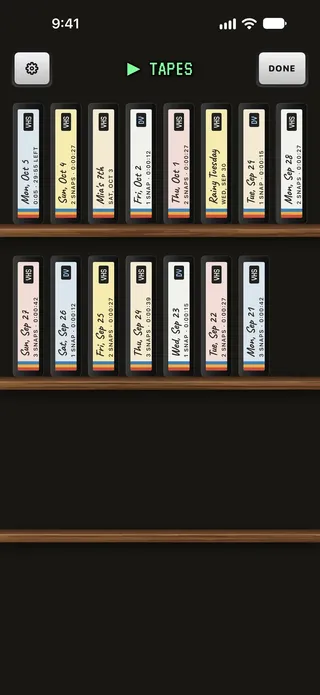 The tape shelf: two wooden shelves of cassettes standing spine-out, each labelled by hand with its day or a name, its snaps and its running time.