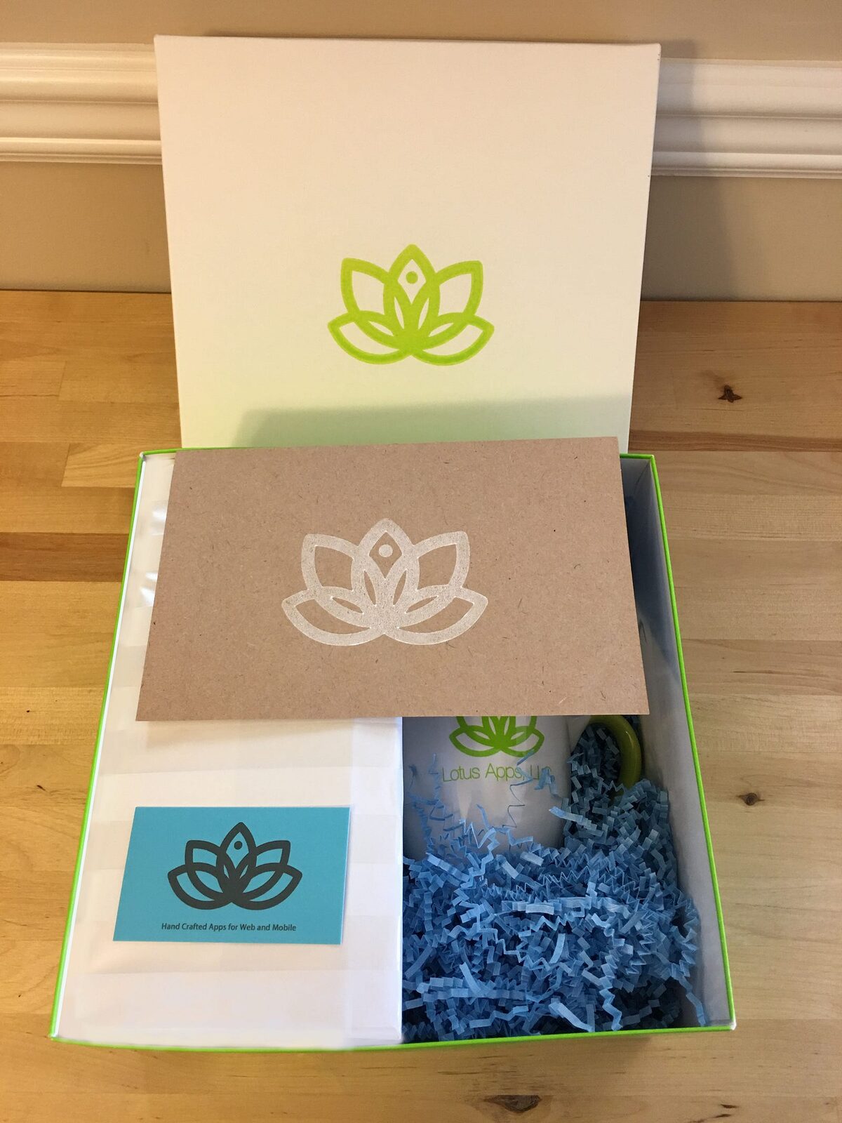 An open gift box holding a stamped card, a business card and a Lotus Apps mug