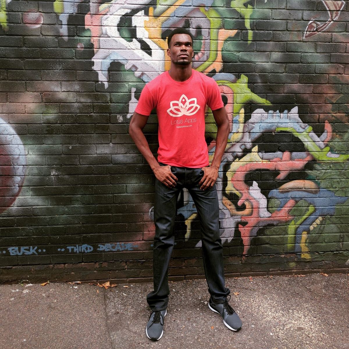 Marcel wearing a red Lotus Apps T-shirt in front of a graffiti wall