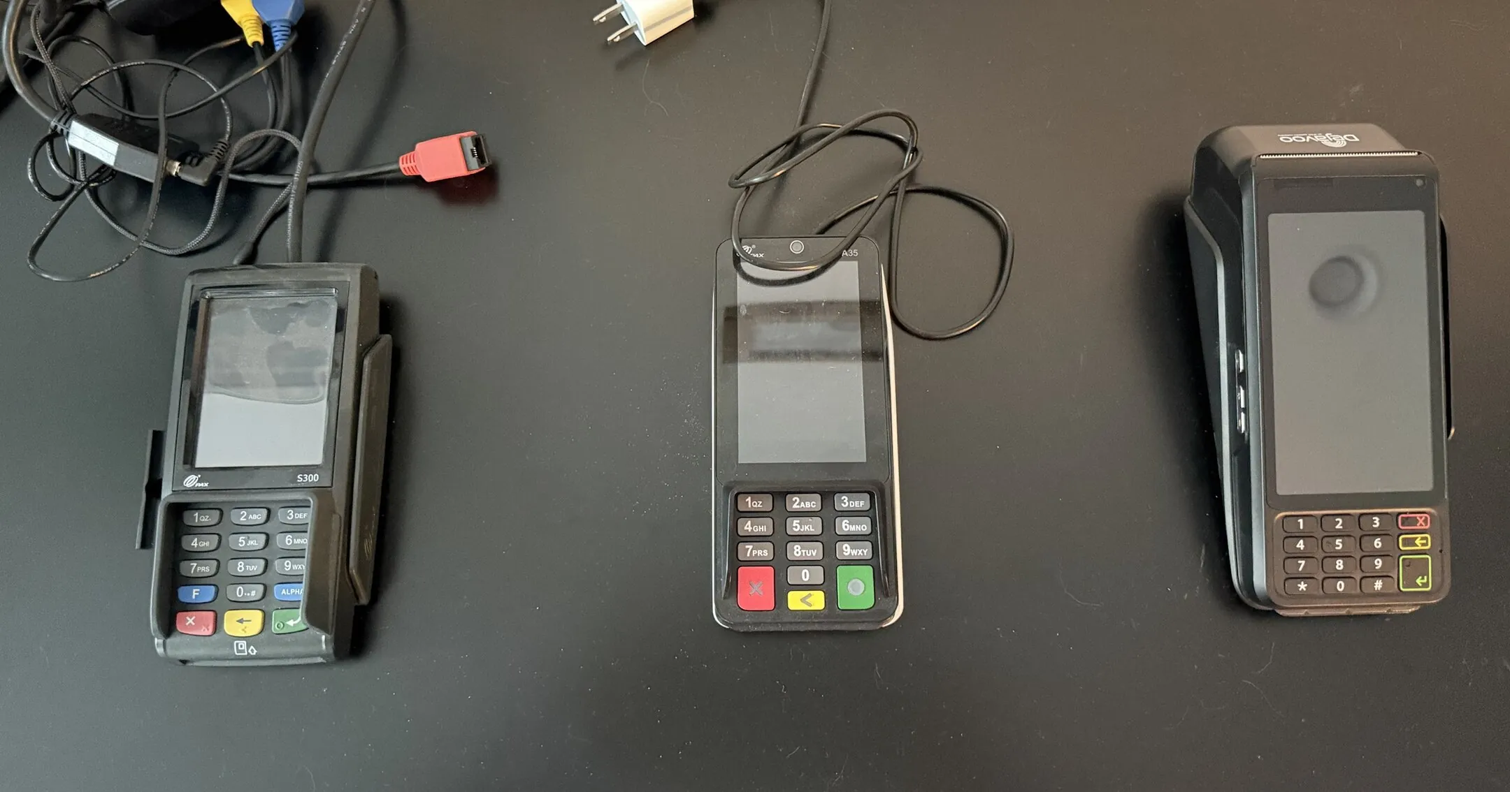 The three card terminals OnTrac has used, from above, oldest on the left. The Heartland terminal has a tangle of cables, the BridgePay one a single cable, and the Dejavoo one none.