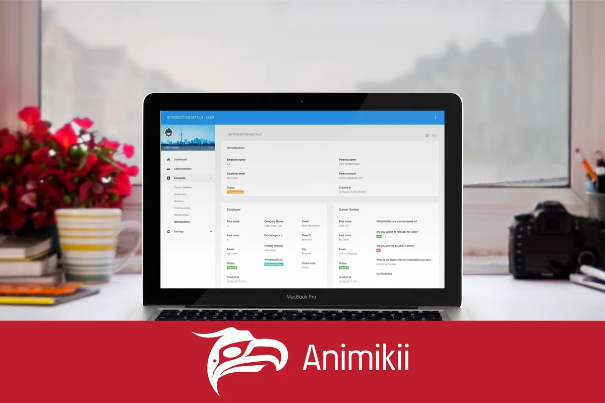 A laptop on a desk showing the AABO admin tool, beside red flowers, above the Animikii logo on red.